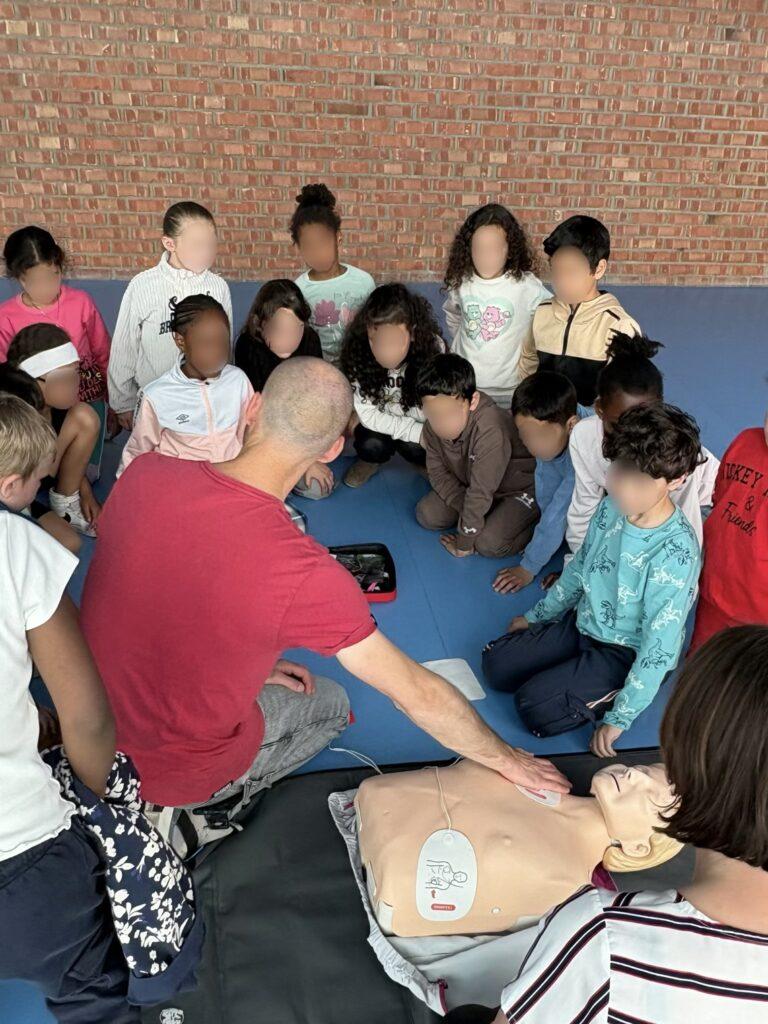 Groupe d'élèves de l'école Voltaire à Amiens assistant à une démonstration de gestes de premiers secours avec un mannequin AmbuMan® et un défibrillateur pédagogique.