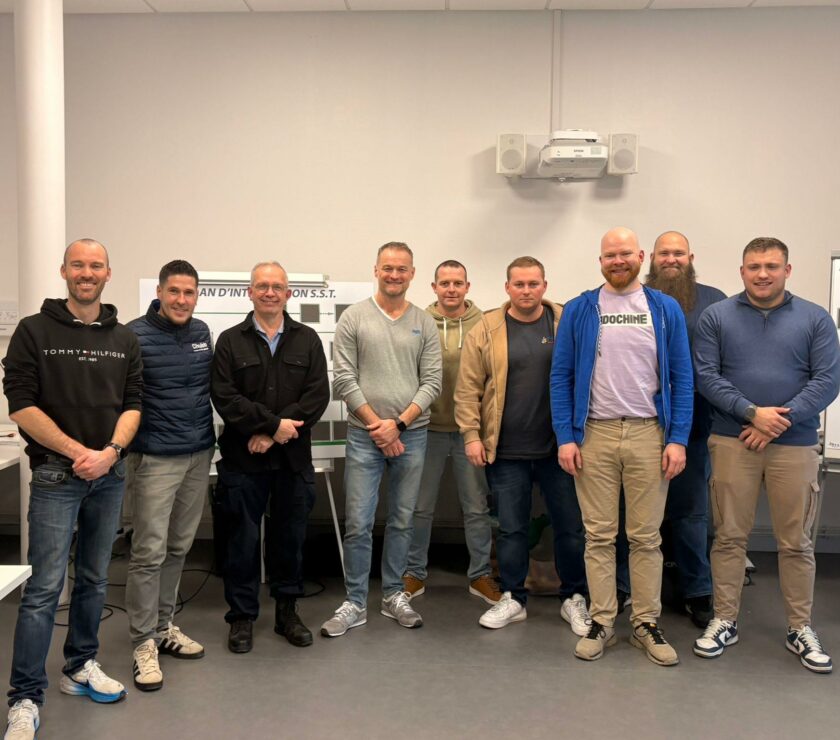 Photo de groupe de neuf hommes souriants posant dans une salle de formation devant des panneaux de 'Plan d'Intervention S.S.T. et de Plan d'Actions Prévention